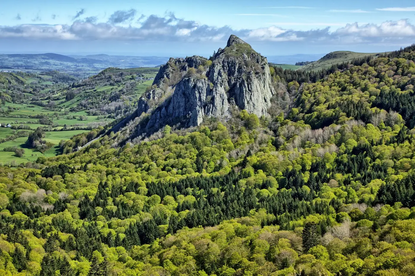 A beautiful aerial view of Roche Sanadoire rock formation, surrounded by lush forests in Auvergne, France.