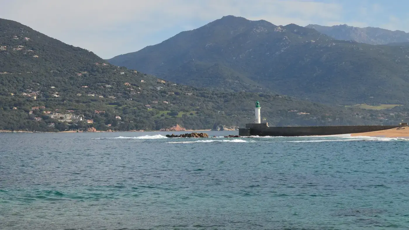 Elegant lighthouse on the coastline of Corsica, France, with rugged mountains in the background.
