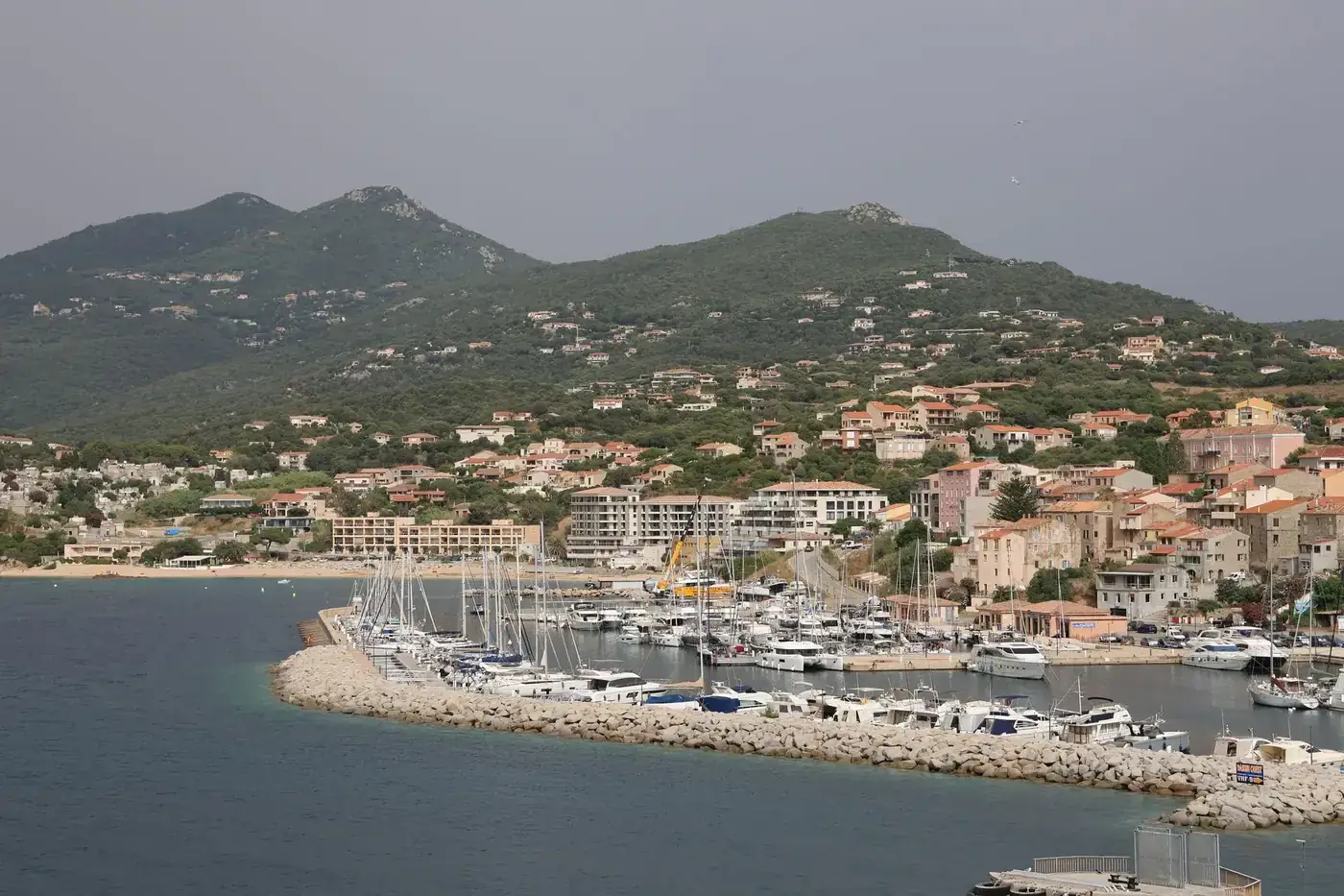 Breathtaking view of a coastal harbor with yachts and lush green hills in the background.