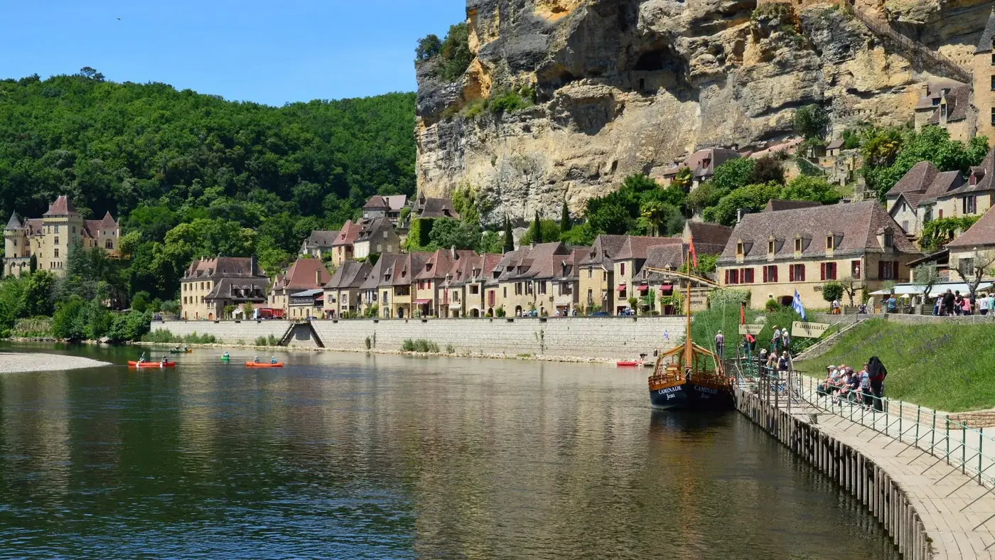 Picturesque riverside village in Dordogne, France with historic buildings and lush greenery.