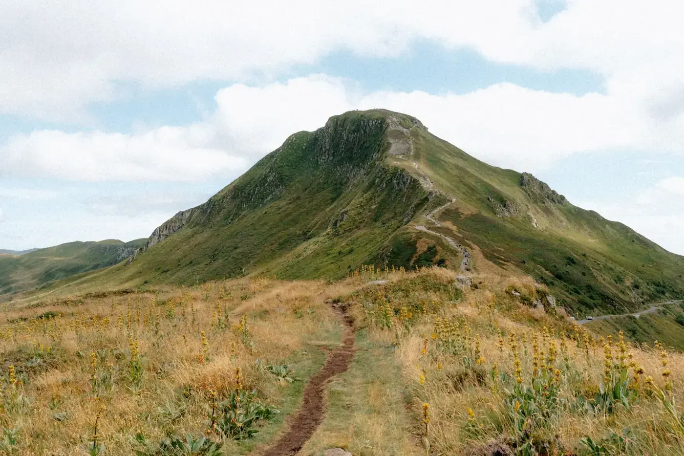 A scenic view of Puy de Sancy mountain with a winding path in Auvergne, France under a blue sky.