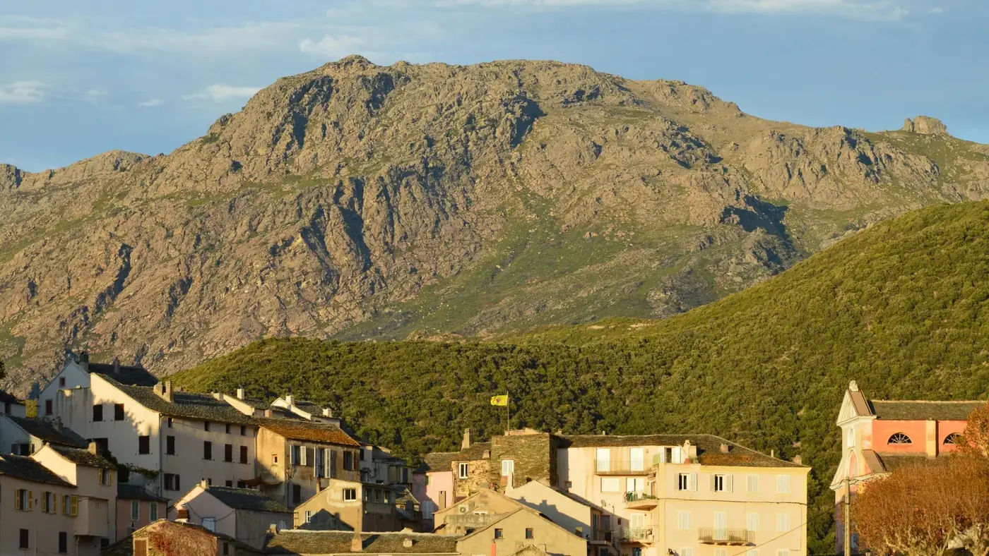Charming view of Nonza, Corsica with mountains and traditional houses.