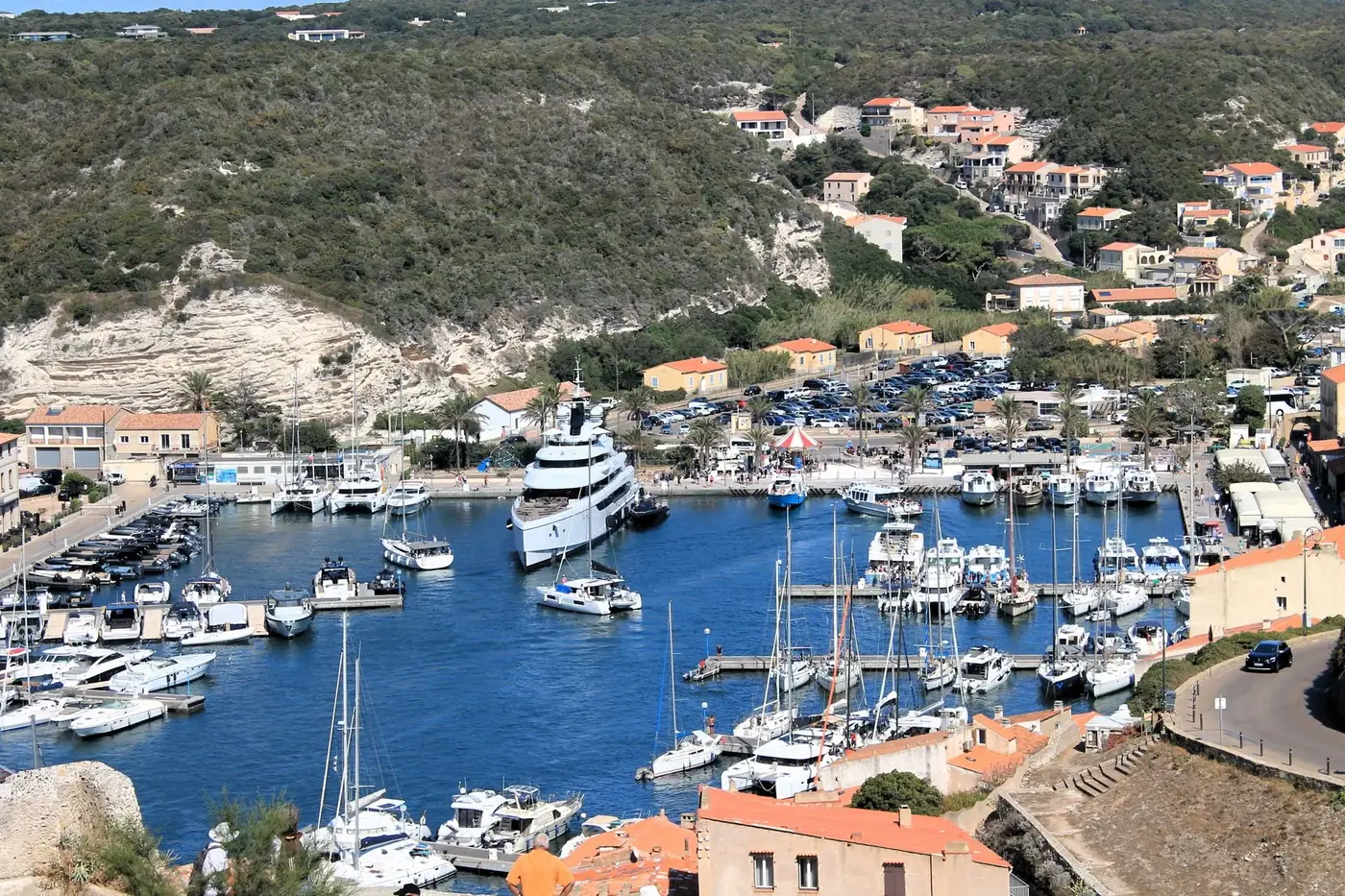 Scenic aerial view of Bonifacio harbor with moored boats and hillside backdrop.