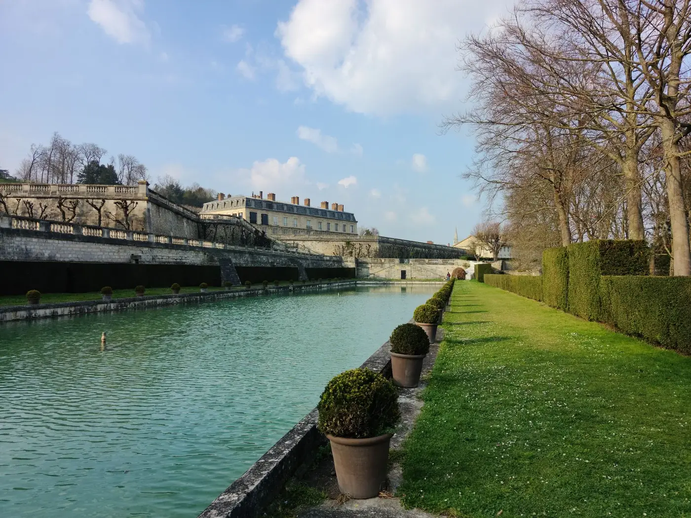 Scenic view of a canal with trees and historic architecture in Saint-Cloud Park, France.