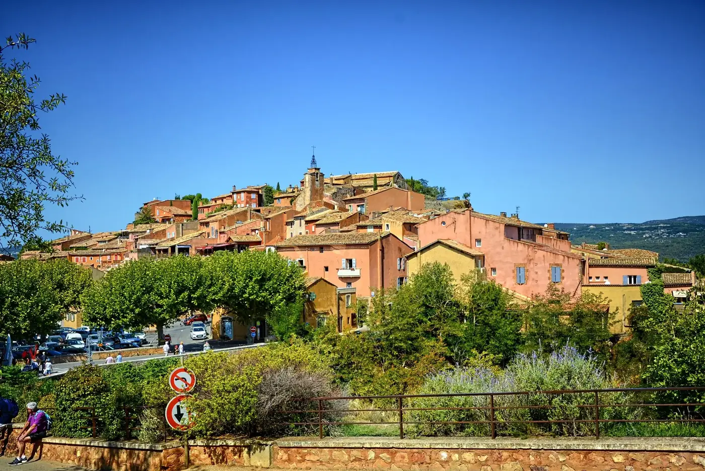 Scenic view of a picturesque hilltop village in Provence, featuring rustic buildings and lush greenery under a clear blu