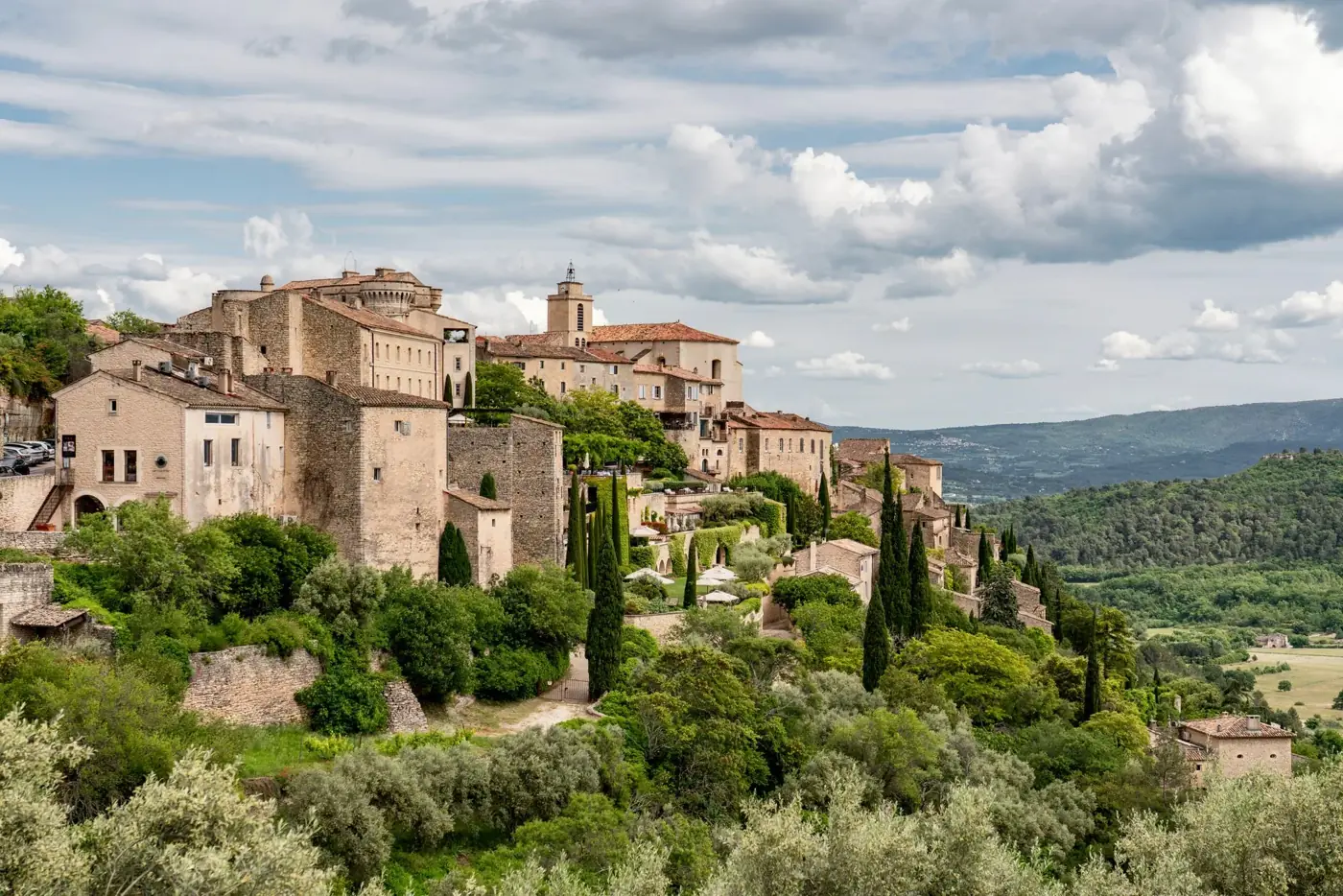Picturesque view of a historic hilltop village in Provence surrounded by lush greenery.