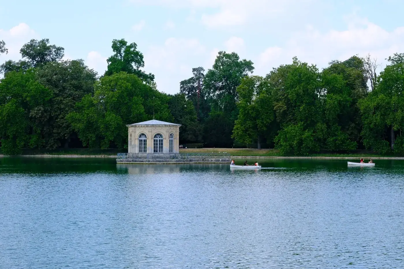 Boaters enjoy a sunny day on the lake at Fontainebleau with lush greenery and historic architecture.