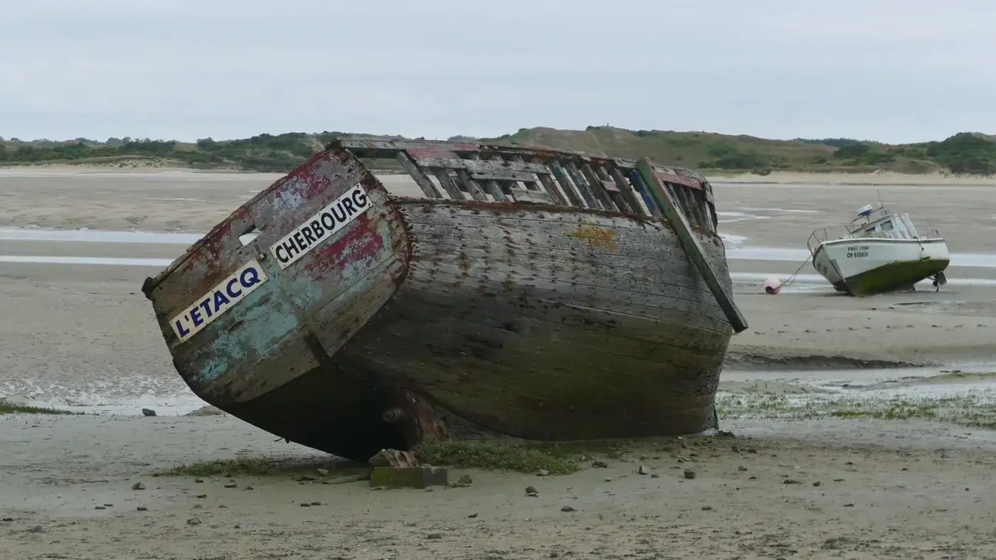 Old wooden boats stranded on sandy shore at Port-Bail-sur-Mer, France.