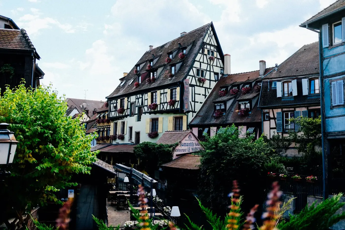 Exterior of historic houses with chimneys located near water canal with wooden walkway among green trees against cloudy