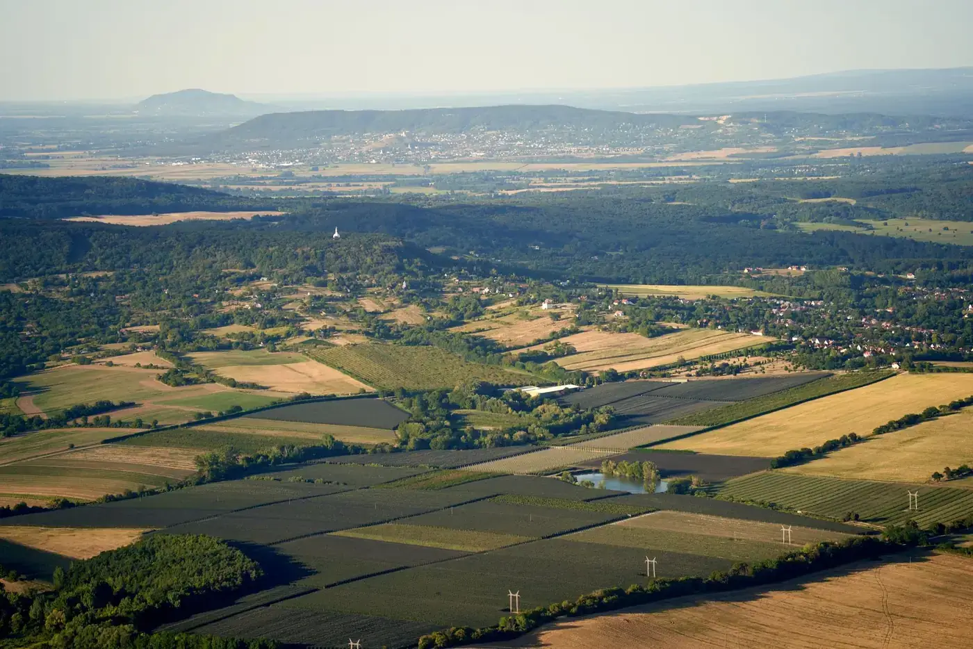 Expansive aerial view showcasing lush green fields, farmland, and distant mountains under daylight.