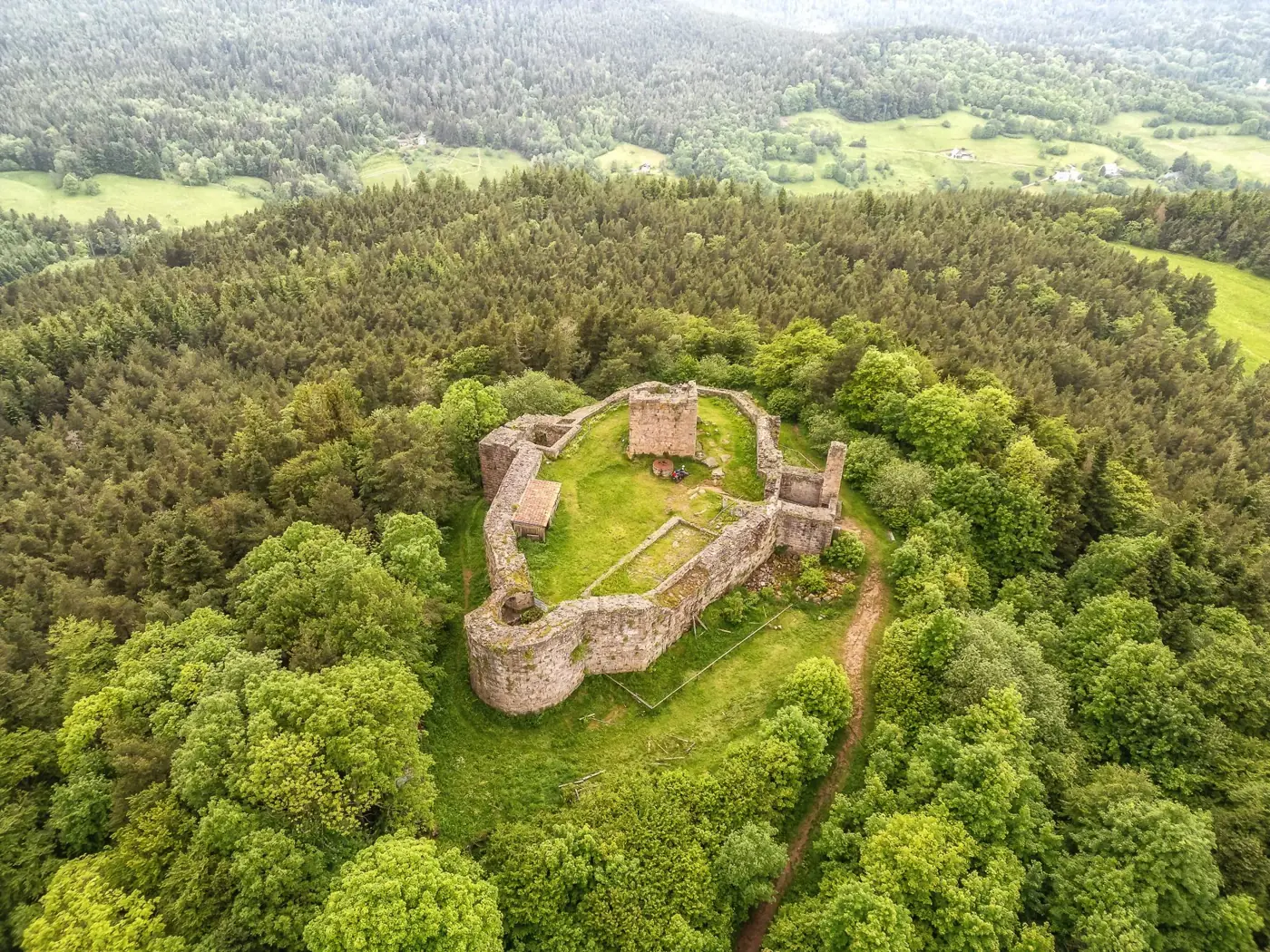 Aerial view of Chateau Des Hohnack surrounded by lush forest in Alsace, France.