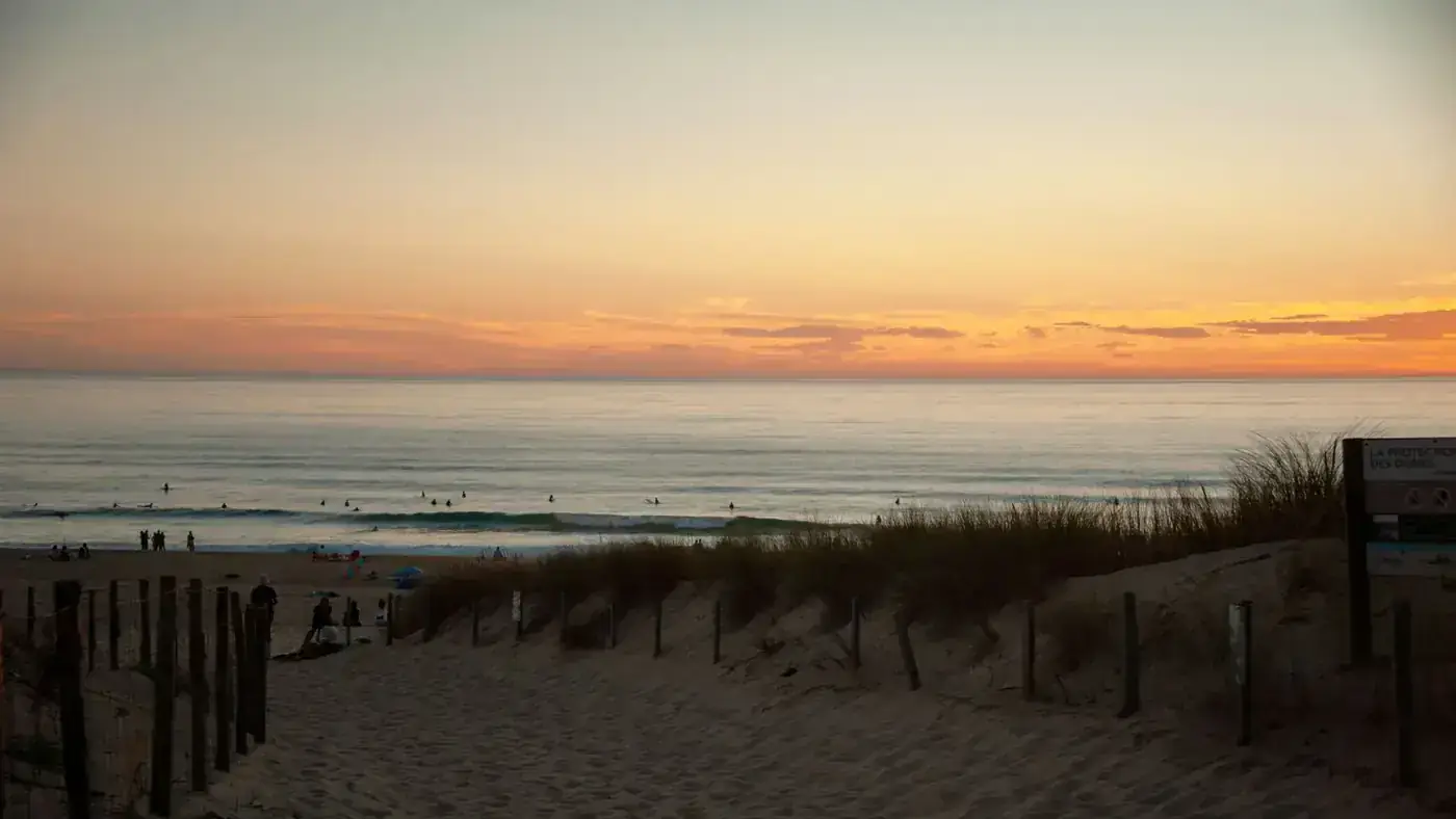Beautiful sunset over Seignosse Beach with surfers enjoying the waves and stunning horizon views.