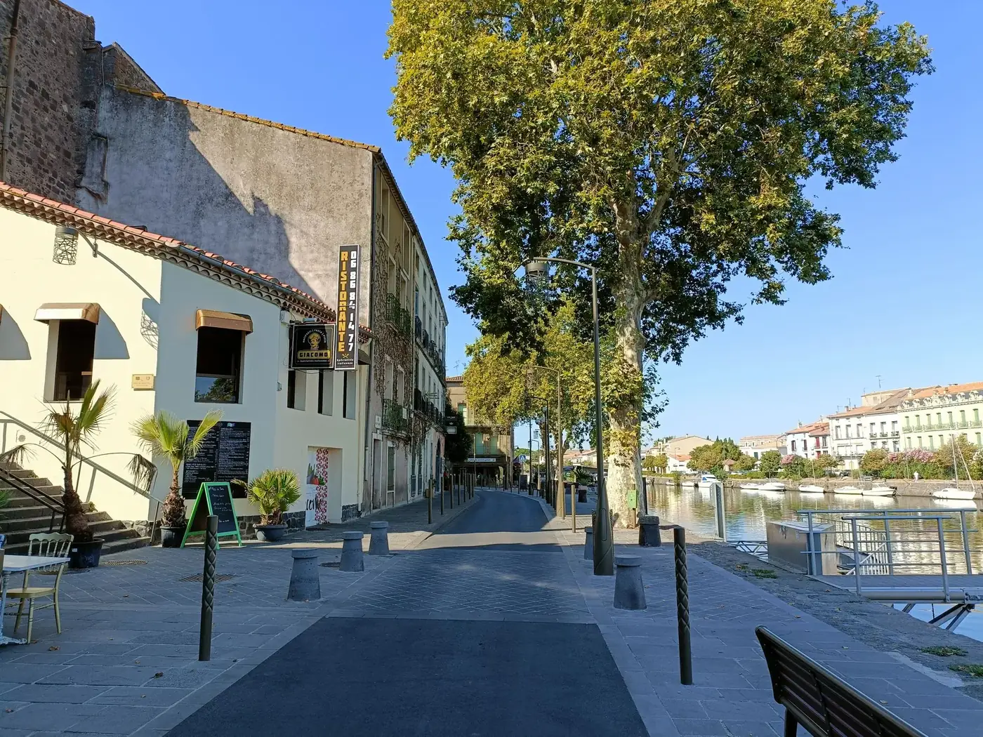 Picturesque view of a quaint riverside street in Agde, Occitanie, France, on a sunny day.