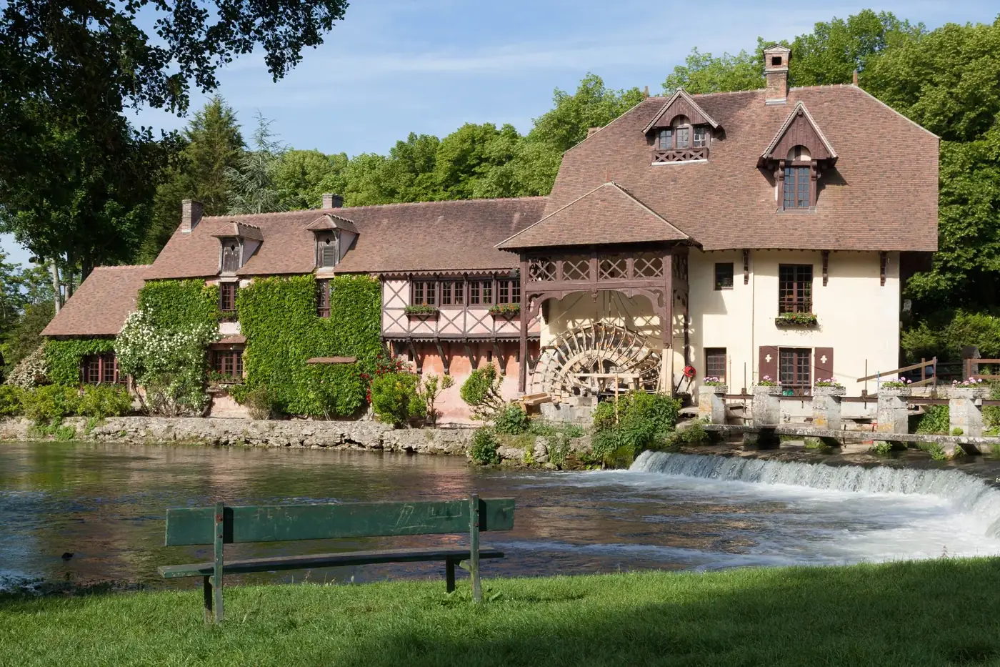 Picturesque historic watermill by a calm river in Gasny, Normandie, surrounded by lush greenery.