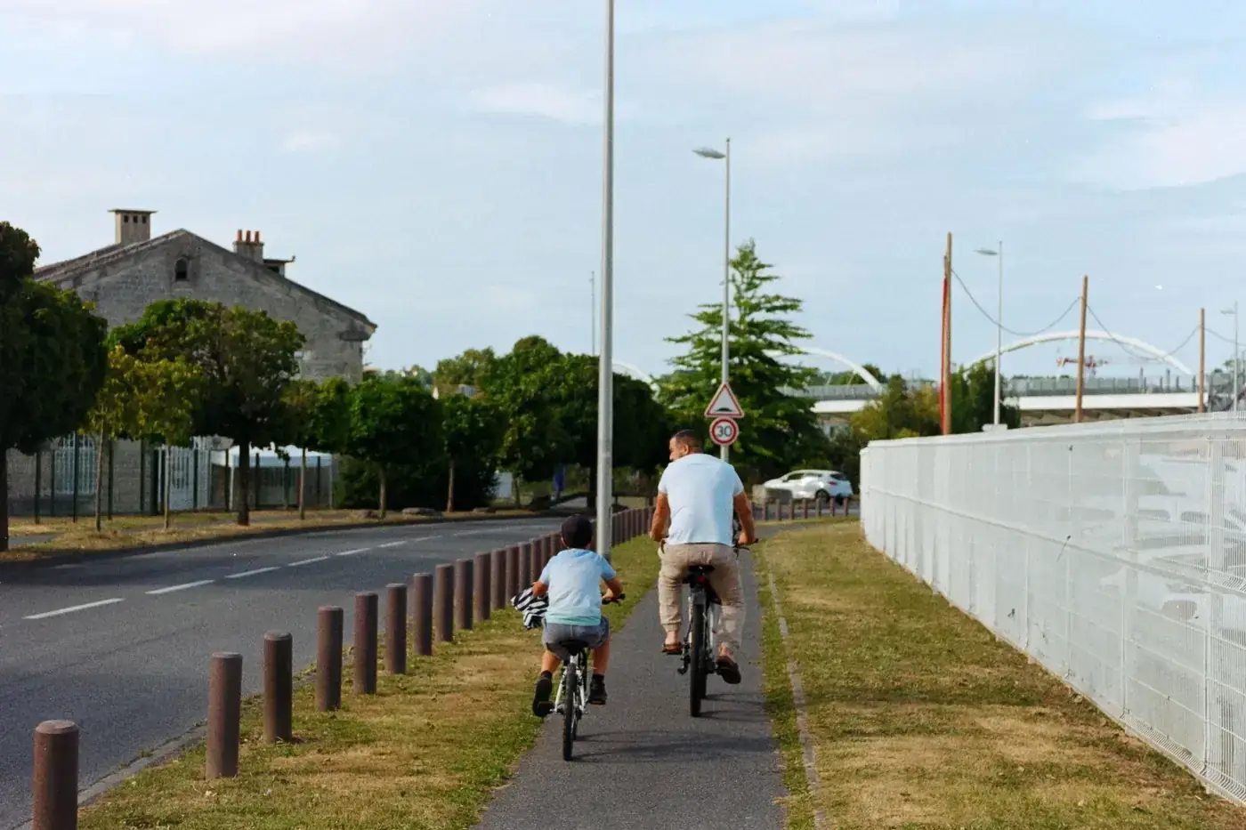 A father and son enjoy cycling on an urban path in a serene summer setting.