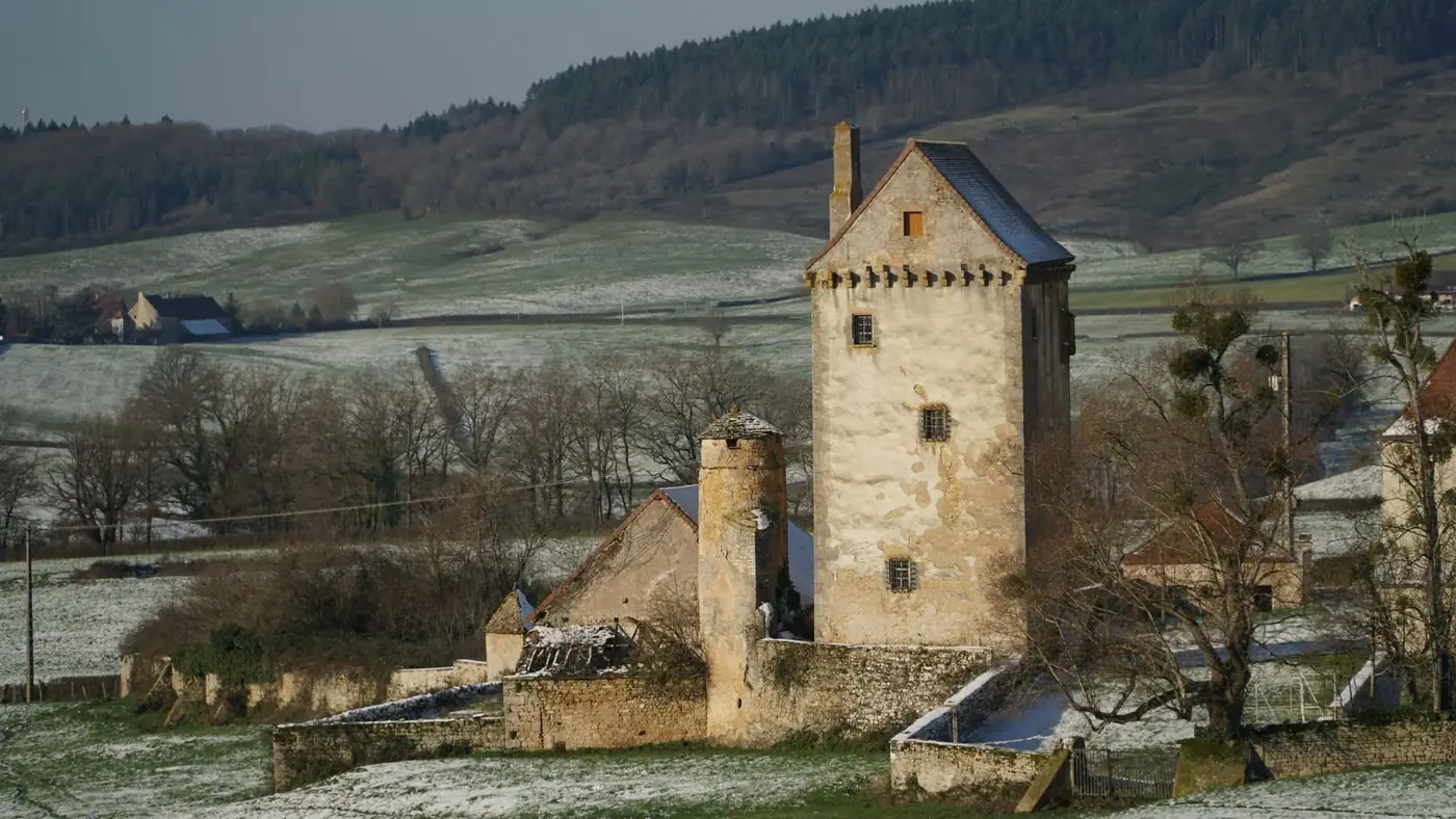A medieval tower stands in a snowy countryside landscape, exuding rustic charm.