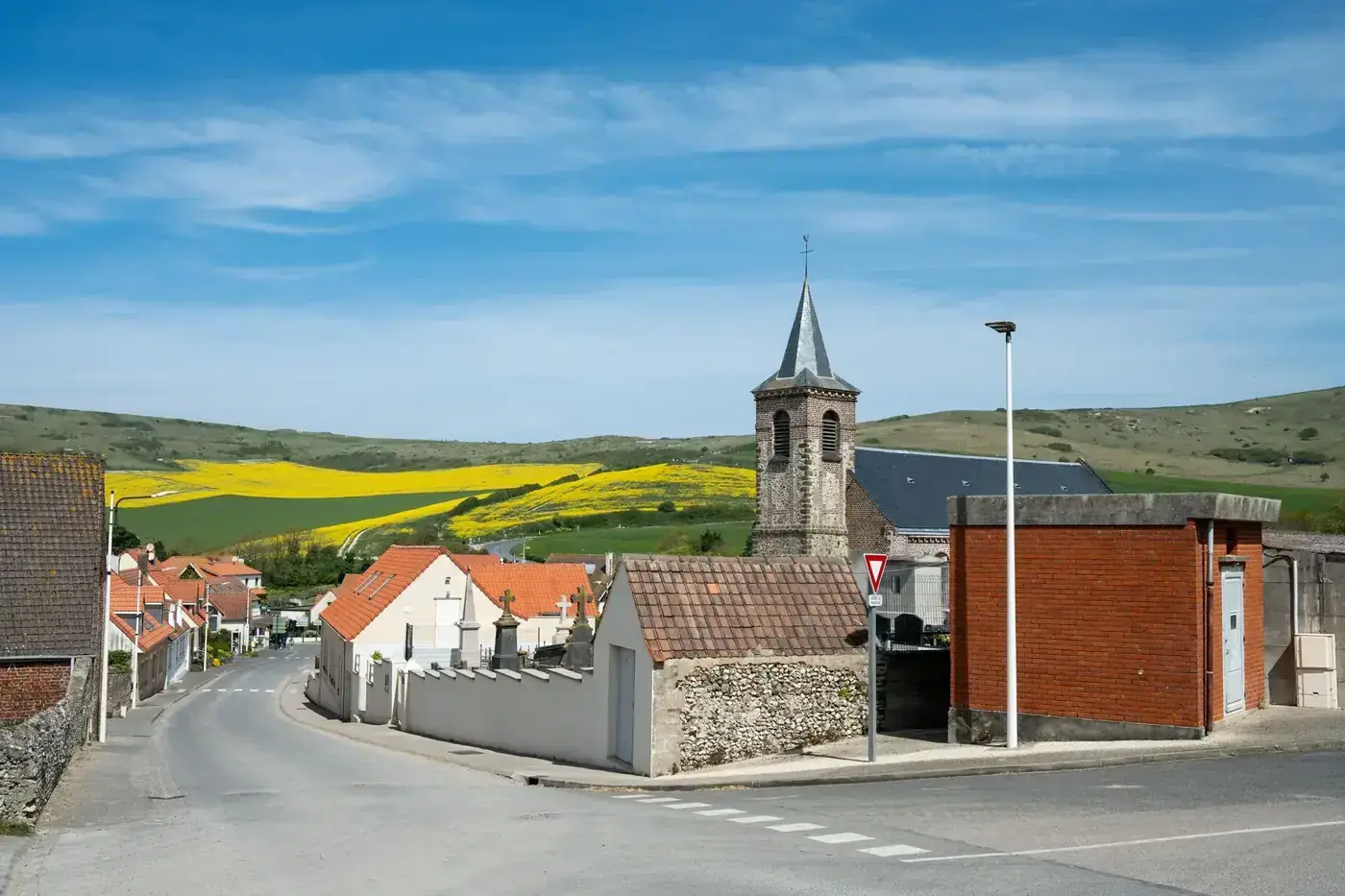 Charming village scene in Escalles, France with church tower and vibrant yellow fields.