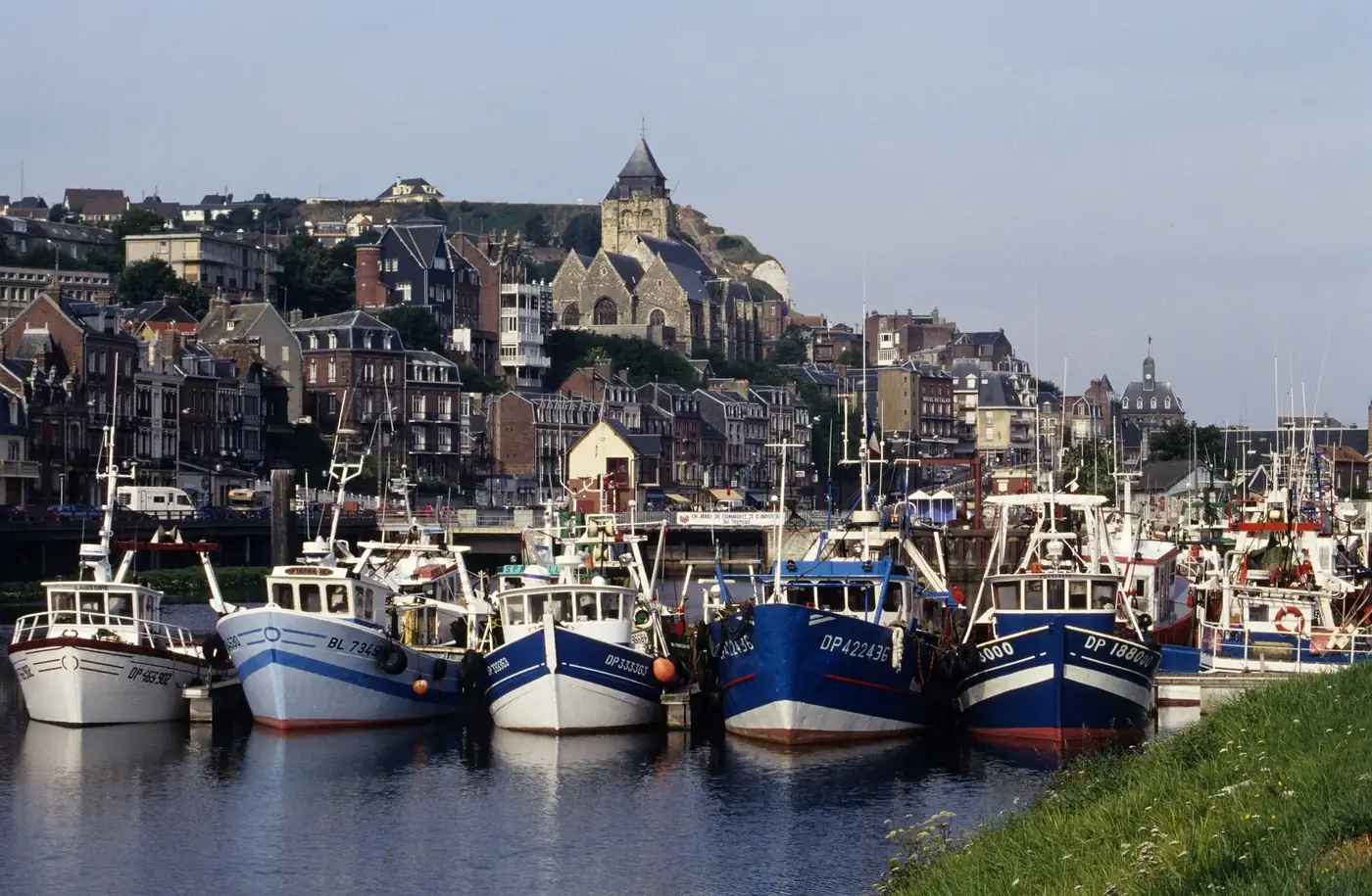 Fishing boats docked in the scenic harbor of Le Tréport, France, with historic town backdrop.