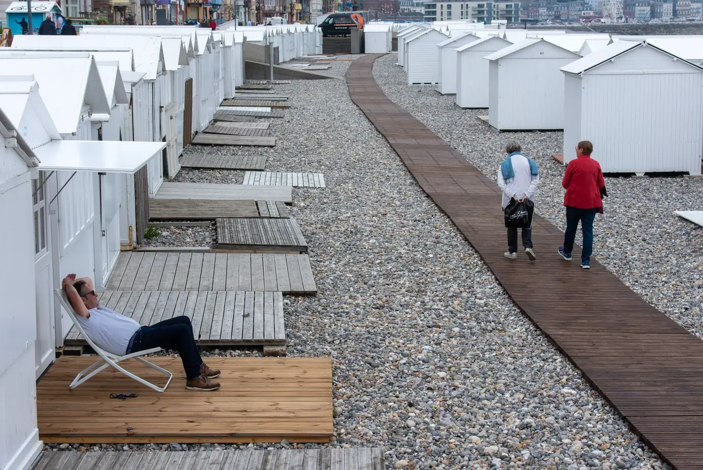 Seaside scene with beach huts and people strolling along the boardwalk in Mers-les-Bains, France.
