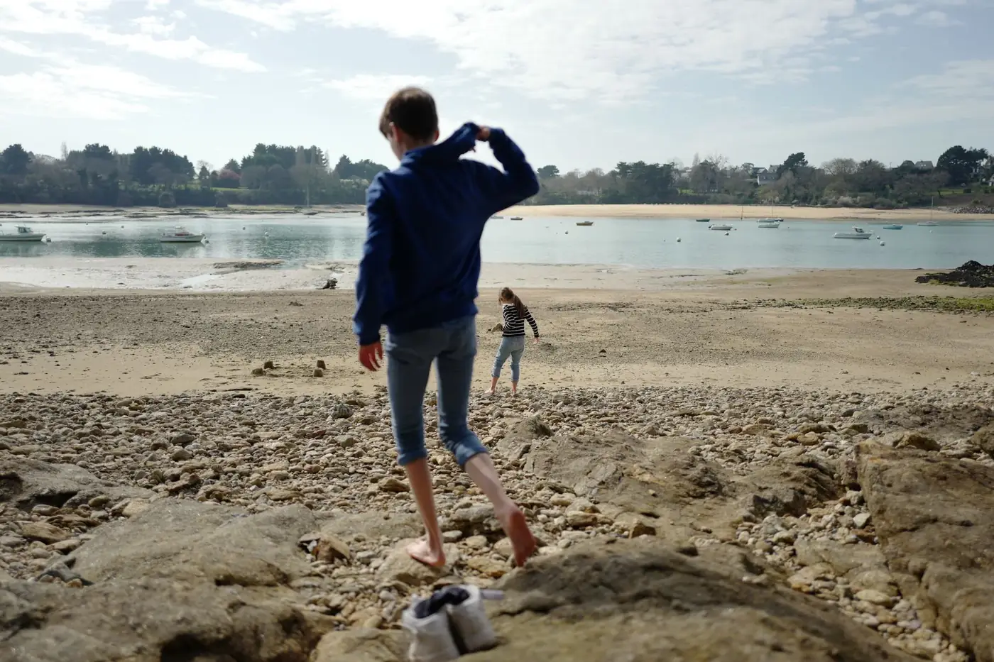 Two people enjoying a stroll on a rocky shore by a serene body of water in France.