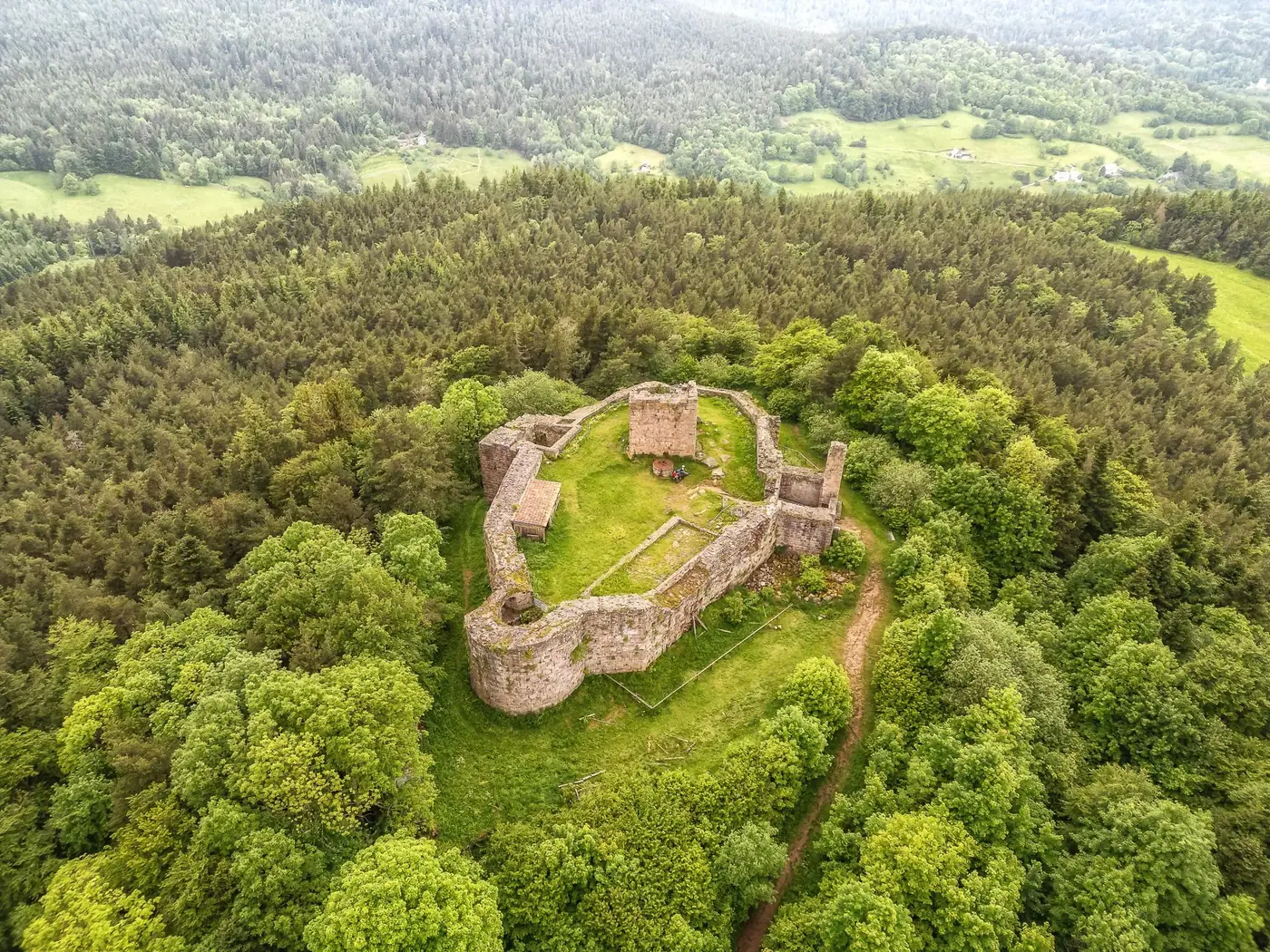 Aerial view of Chateau Des Hohnack surrounded by lush forest in Alsace, France.